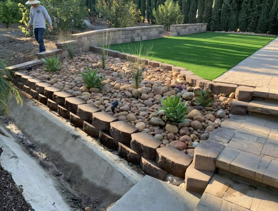 Block retaining walls with a rock bed, succulents and new turf on the upper level