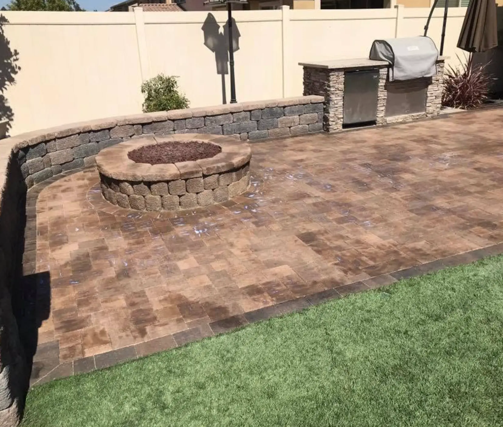 Round stone fire pit with a curved seat wall and a built-in BBQ island on a paver patio