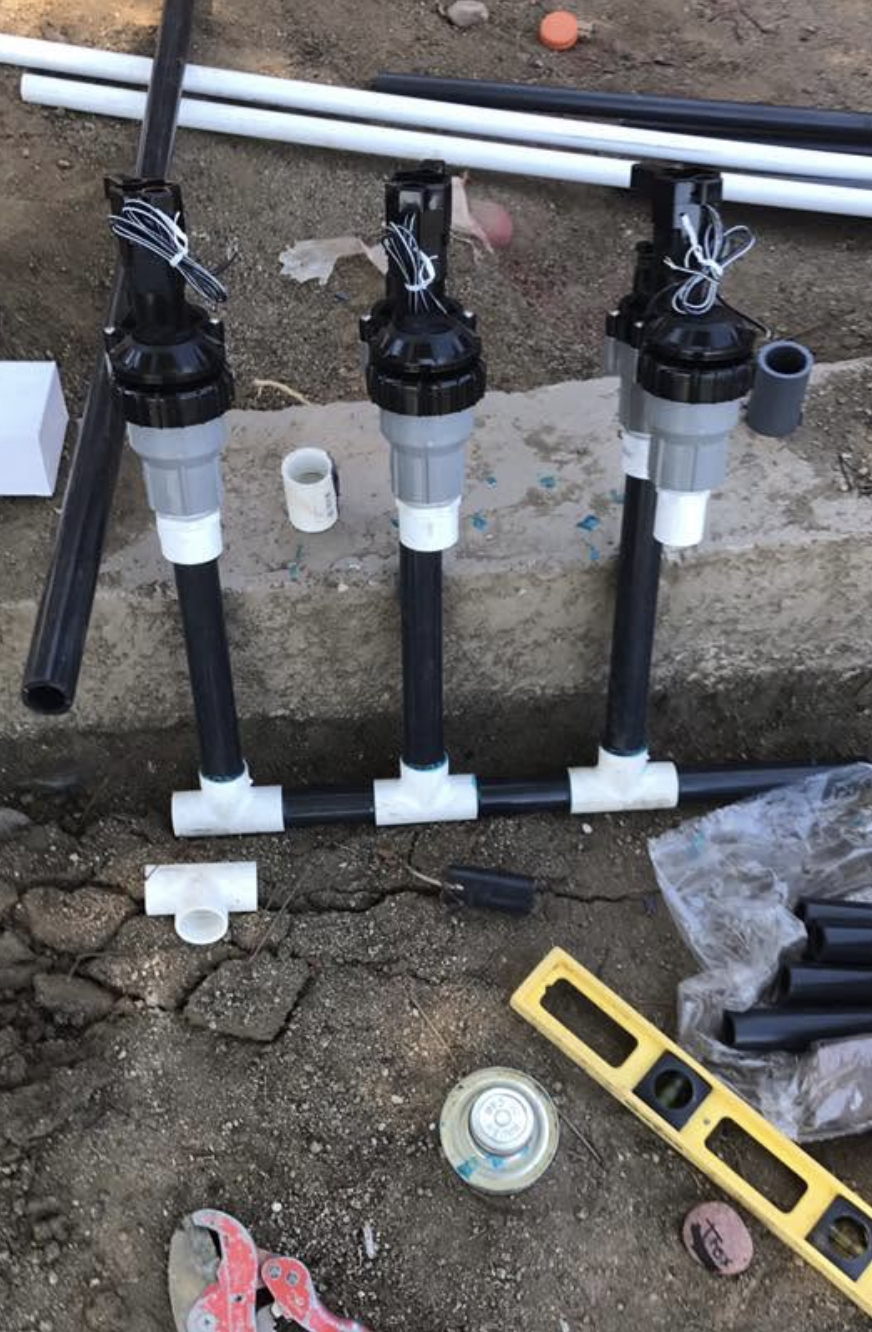 Irrigation valve manifold being assembled with PVC fittings and tools on a job site