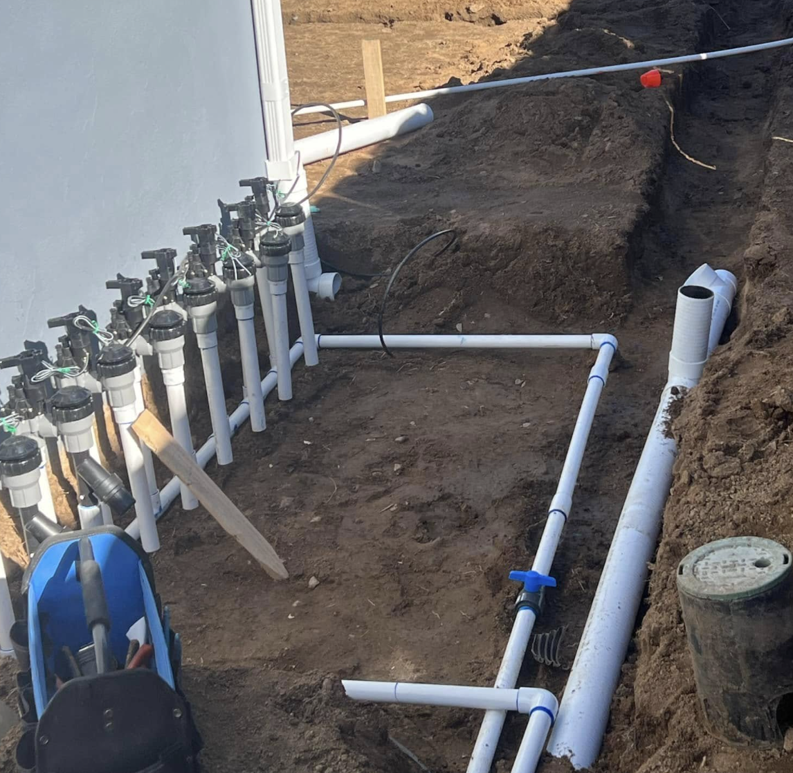 Full irrigation manifold and PVC piping being installed in a trenched yard
