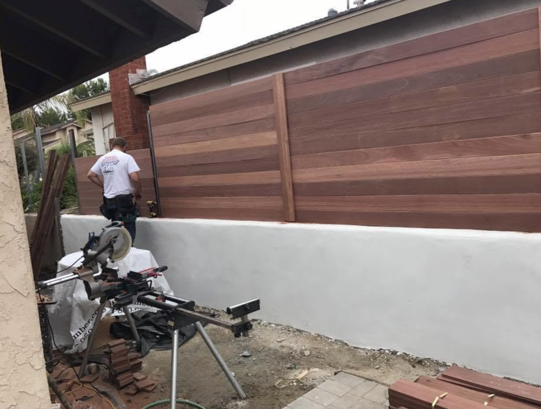 Crew installing a horizontal wood fence above a stucco wall with a miter saw on site