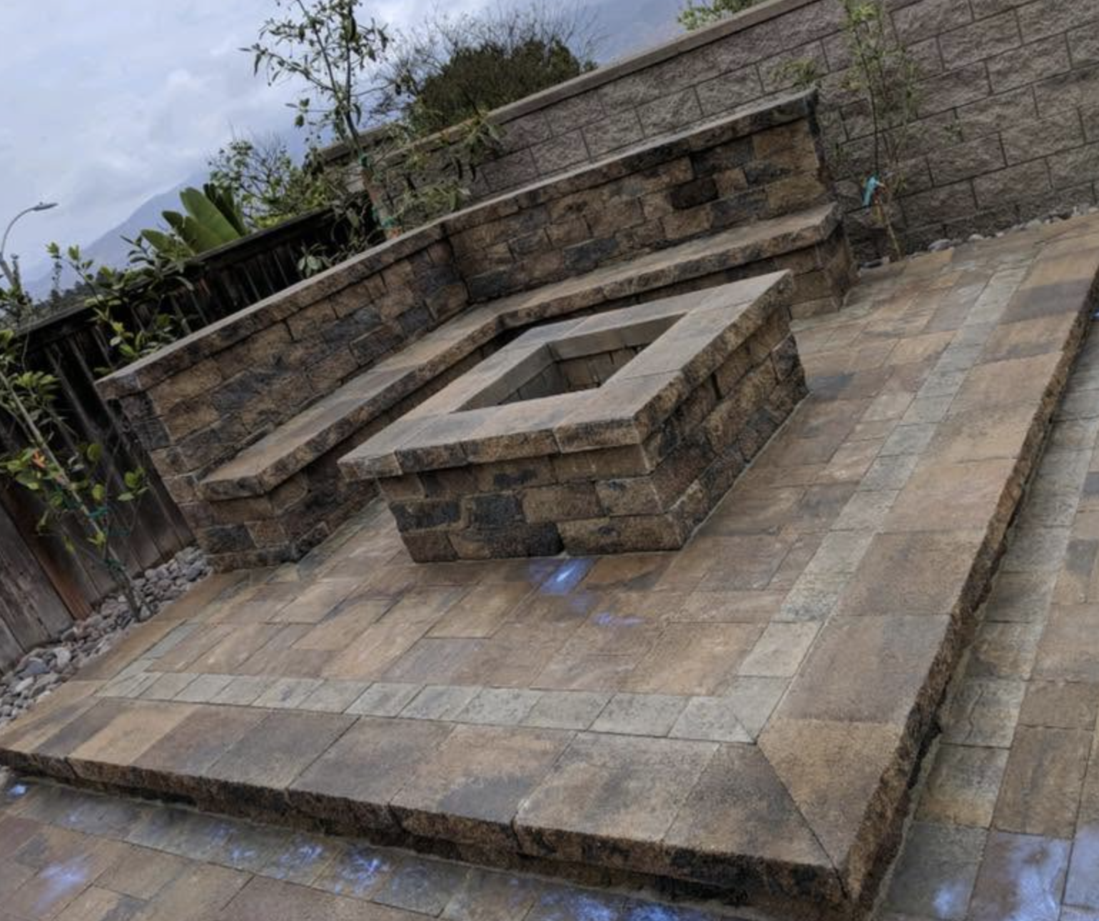 Stone retaining wall with a built-in raised fire pit feature on a paver patio