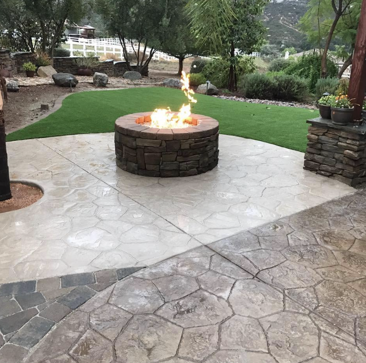 Stone fire pit on a stamped concrete and paver patio with fresh turf beyond