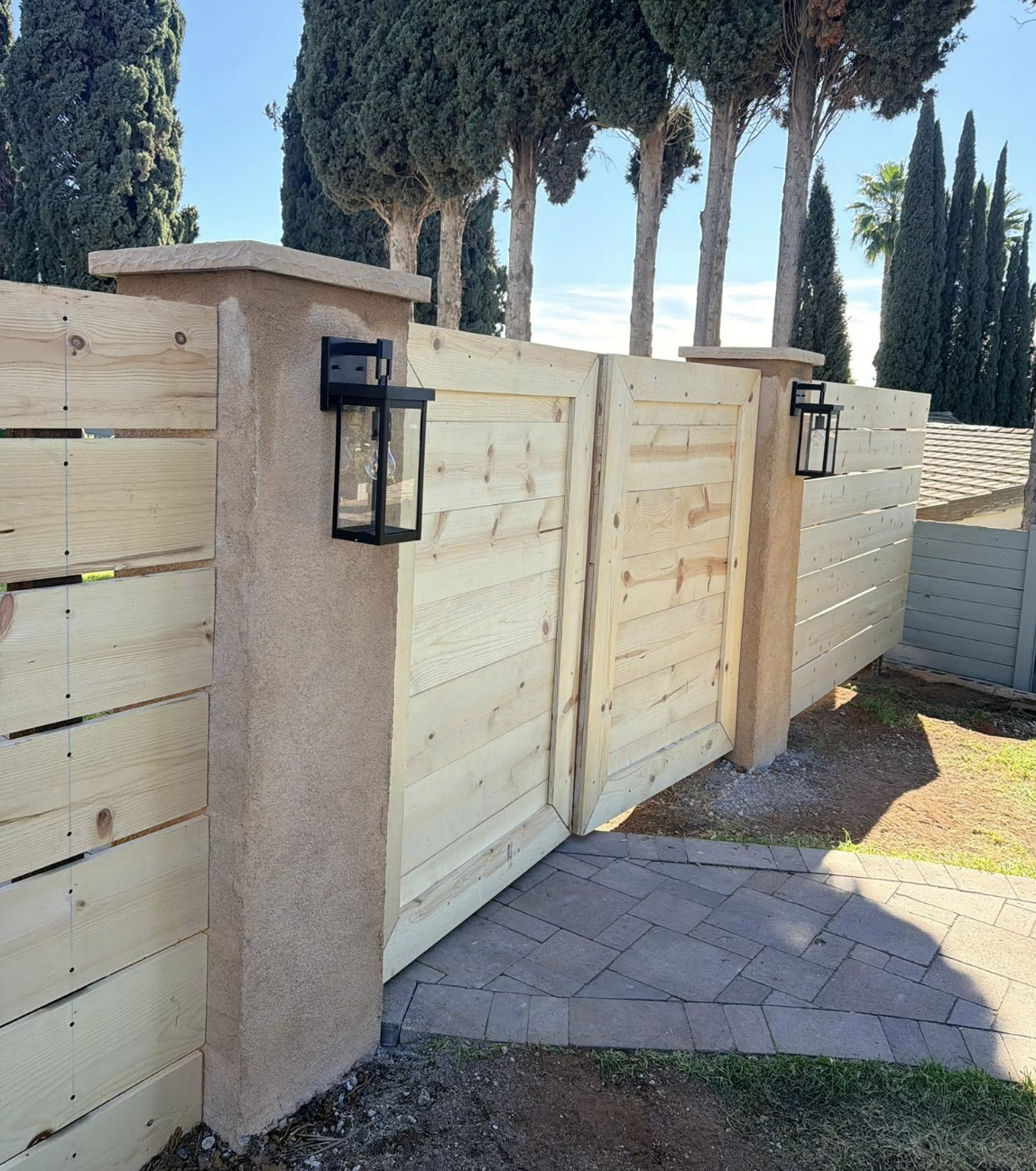 New horizontal wood fence and double gate between stucco pillars with lantern lights